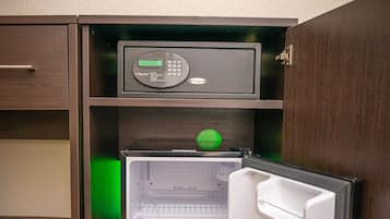 Un refrigerador compacto en una pequeña cocina, con un microondas encima y un cuadro en la pared.