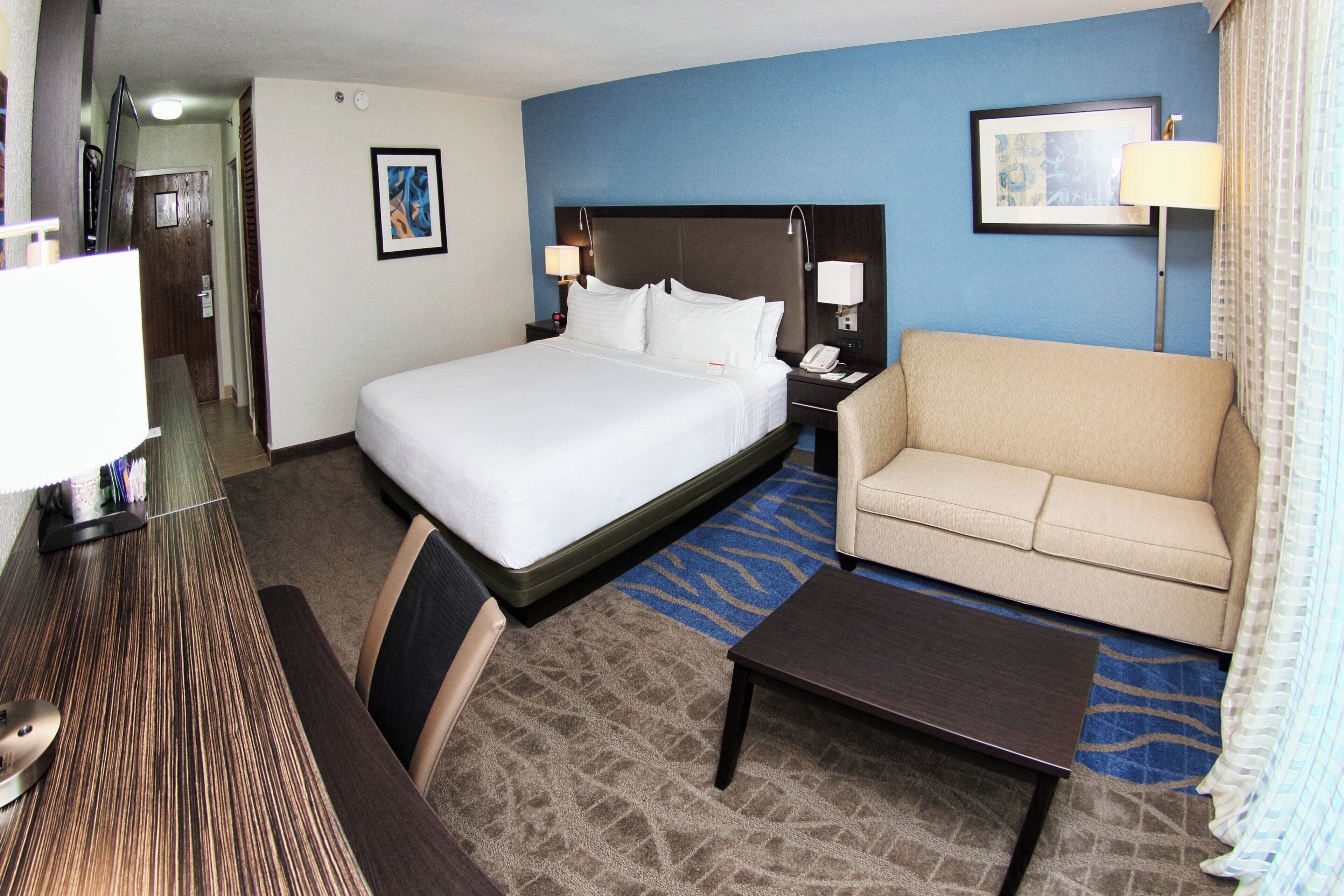 Una habitación de hotel con una cama, un sofá, un escritorio y una mesita de noche con lámpara.