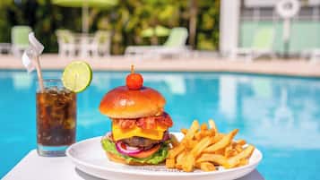 Hamburguesa con papas fritas y un refresco junto a una piscina.