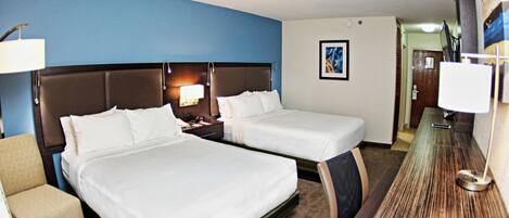 A hotel room with two beds, a desk, a chair, a lamp, and a painting on the wall.