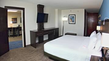 A hotel room with a bed, desk, chair, television, and a desk lamp.