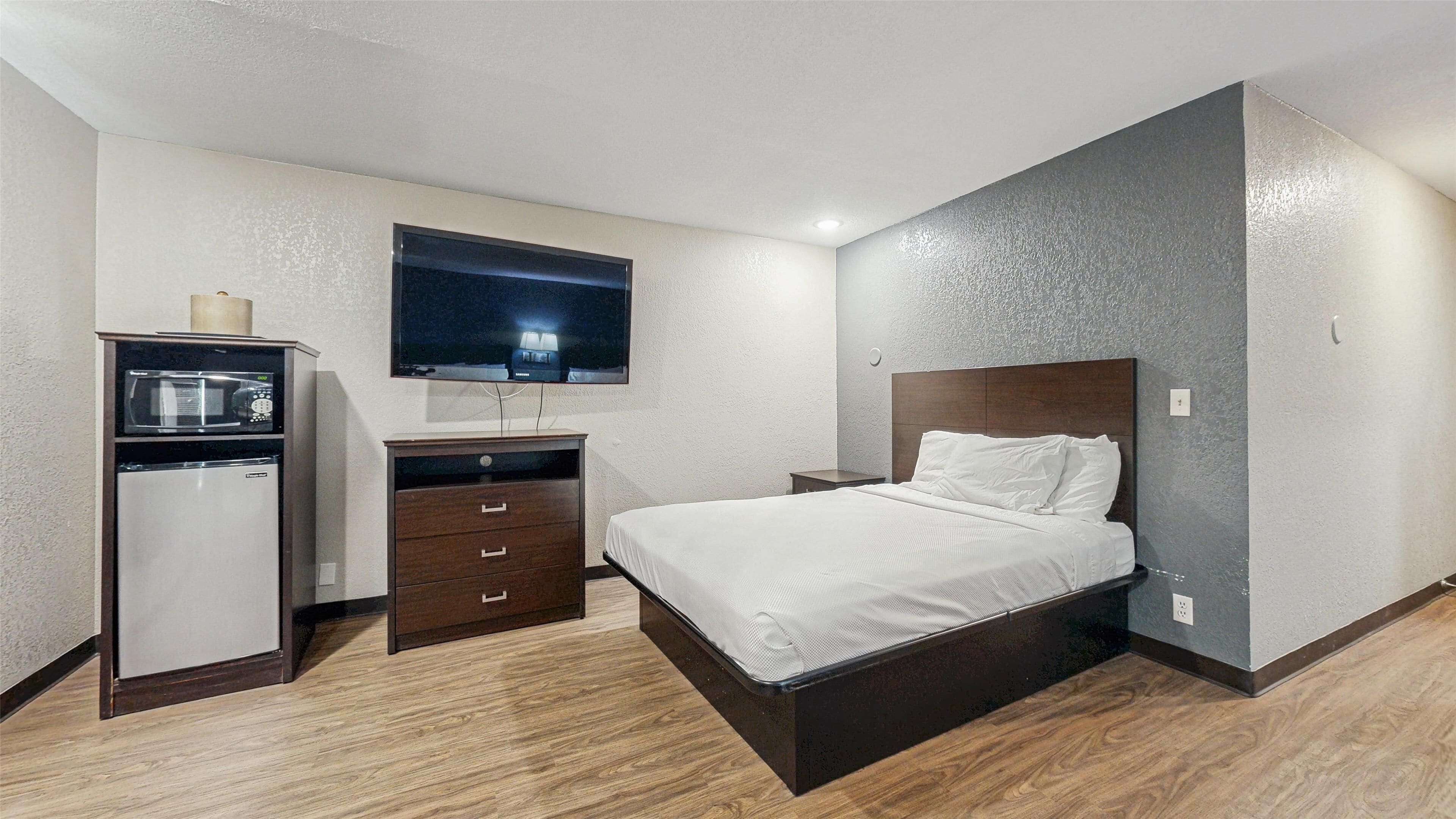 A bedroom with a bed, a dresser, a microwave, and a television.