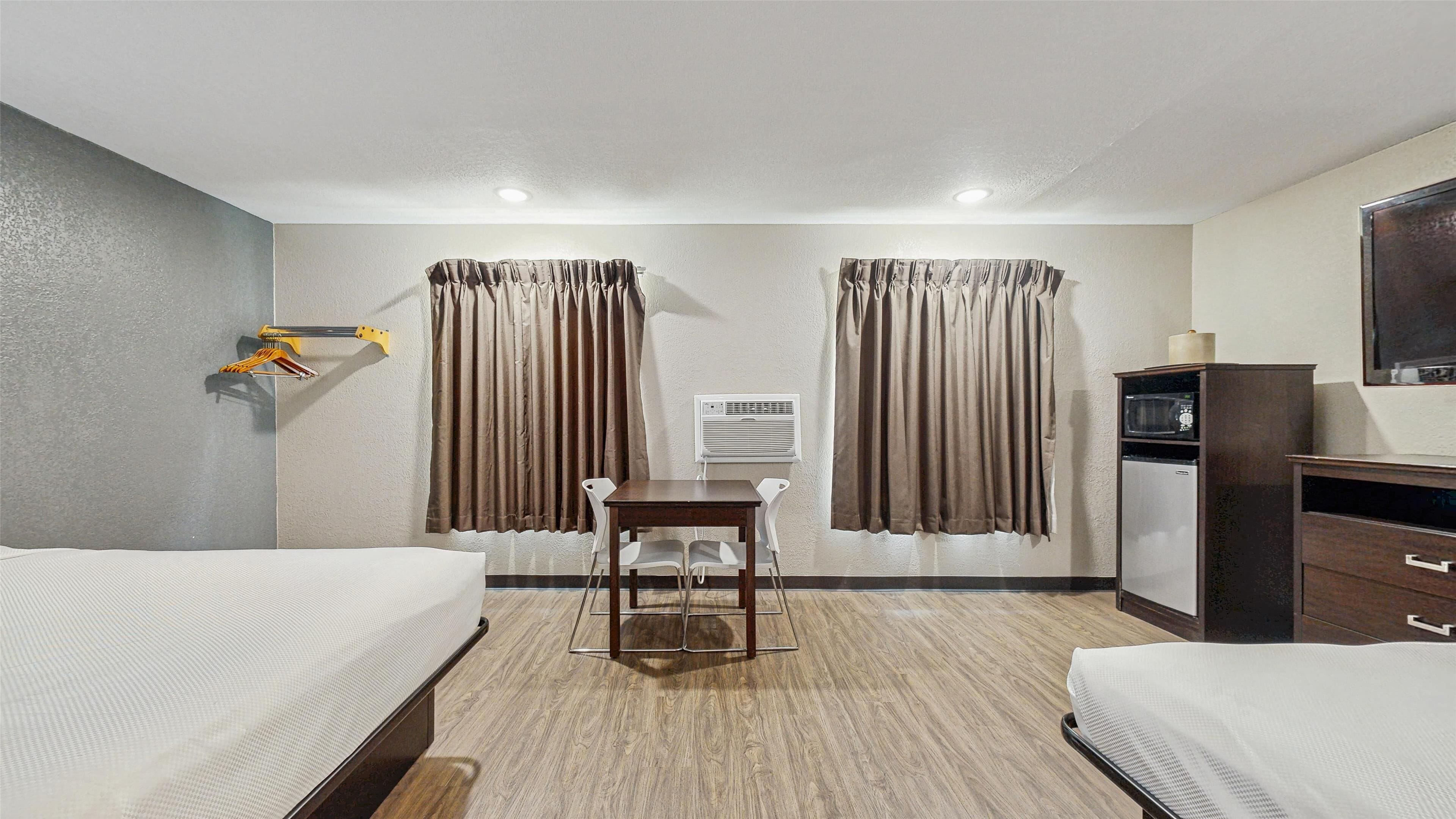 A hotel room with two beds, a desk, a chair, a TV, and a minibar.