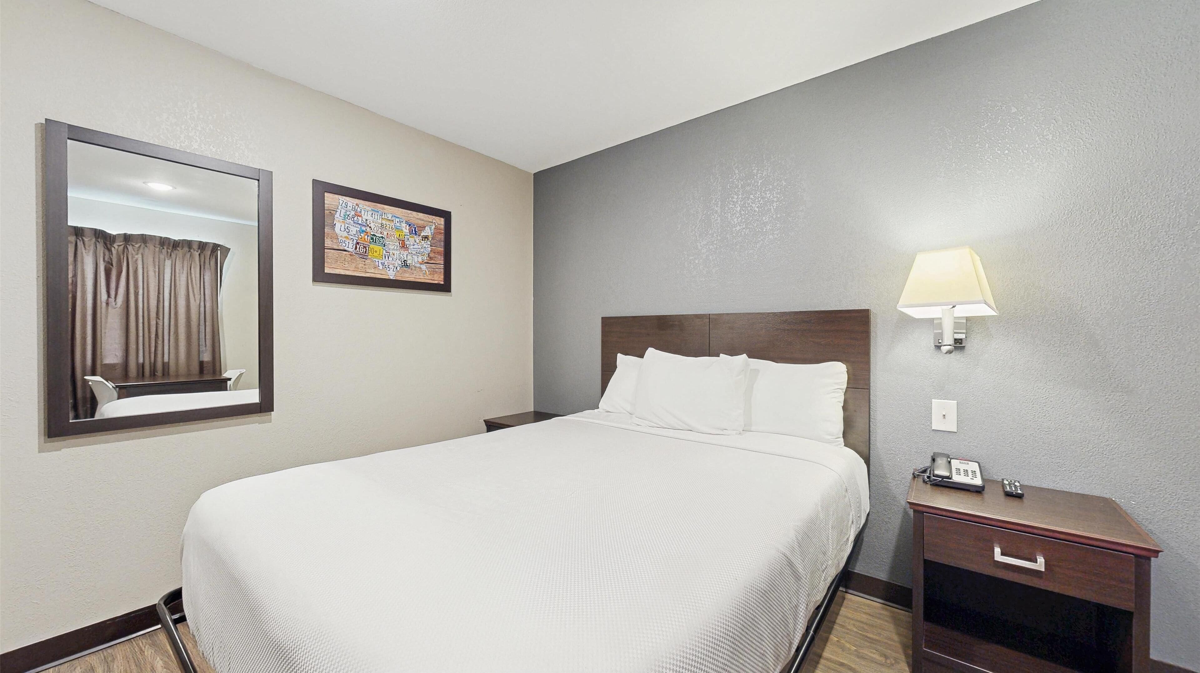 A hotel room with a large bed, a nightstand with a lamp, a mirror, and a wall-mounted map.