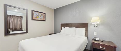 A hotel room with a large bed, a nightstand with a lamp, a mirror, and a wall-mounted map.