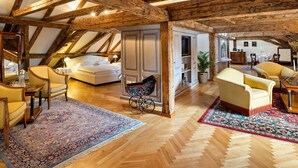 A spacious loft with exposed wooden beams, a large bed, a dining area, and a view through the skylight. - Radisson Blu Hotel Altstadt (Salzburg)