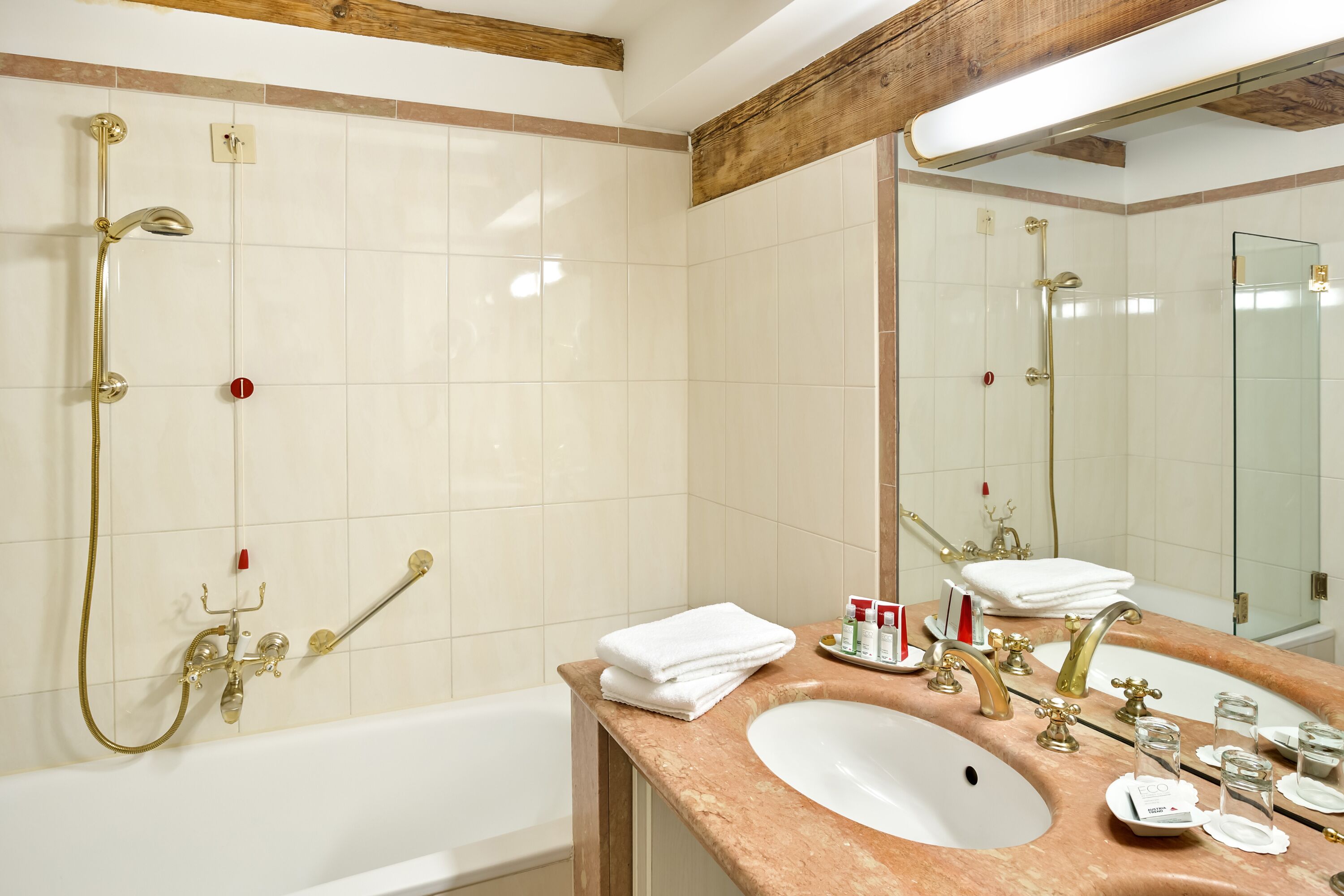 Une salle de bain avec une baignoire, un lavabo avec un miroir et une douche avec des accessoires dorés.