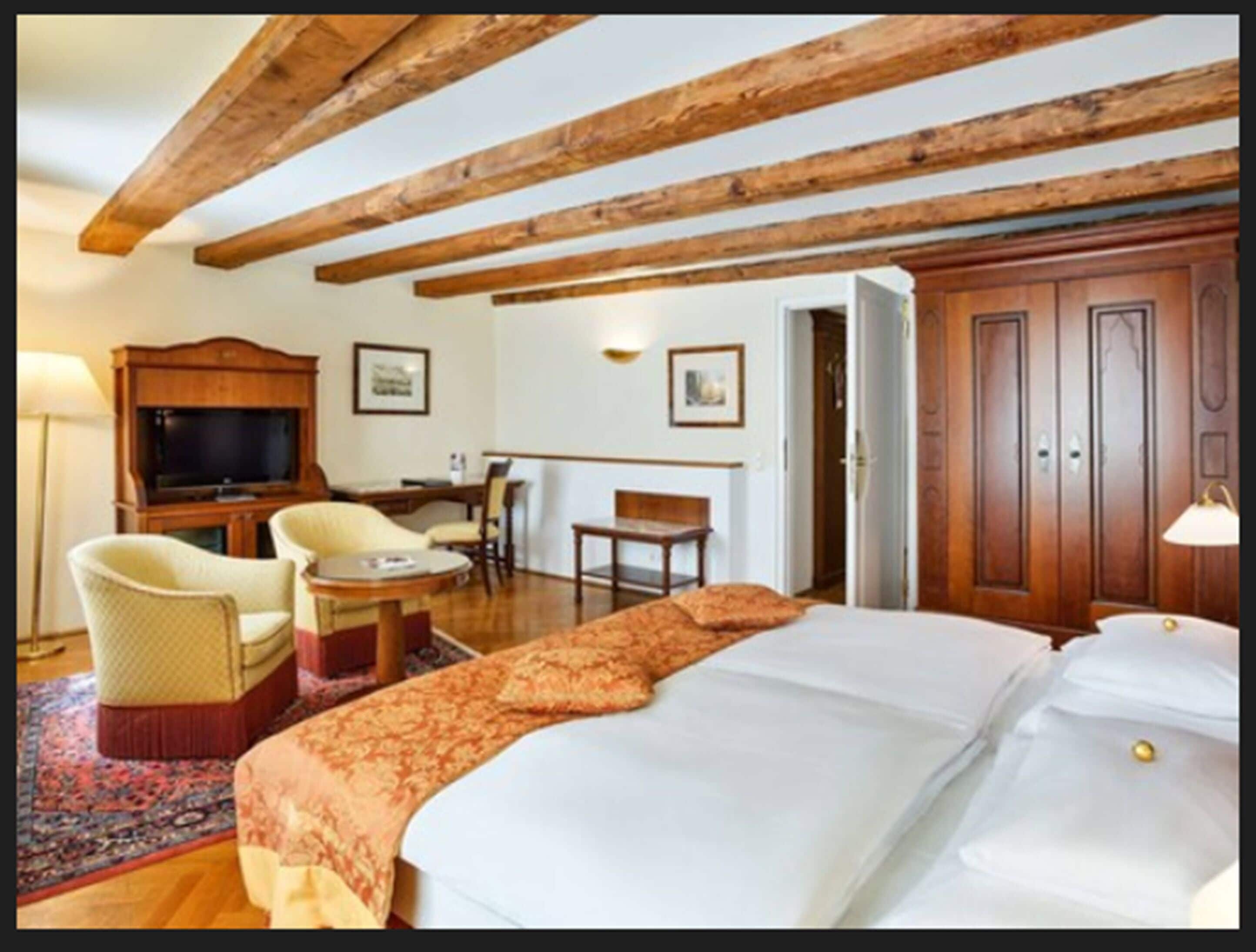 A hotel room with a large bed, a desk, two chairs, a television, and wooden beams on the ceiling.