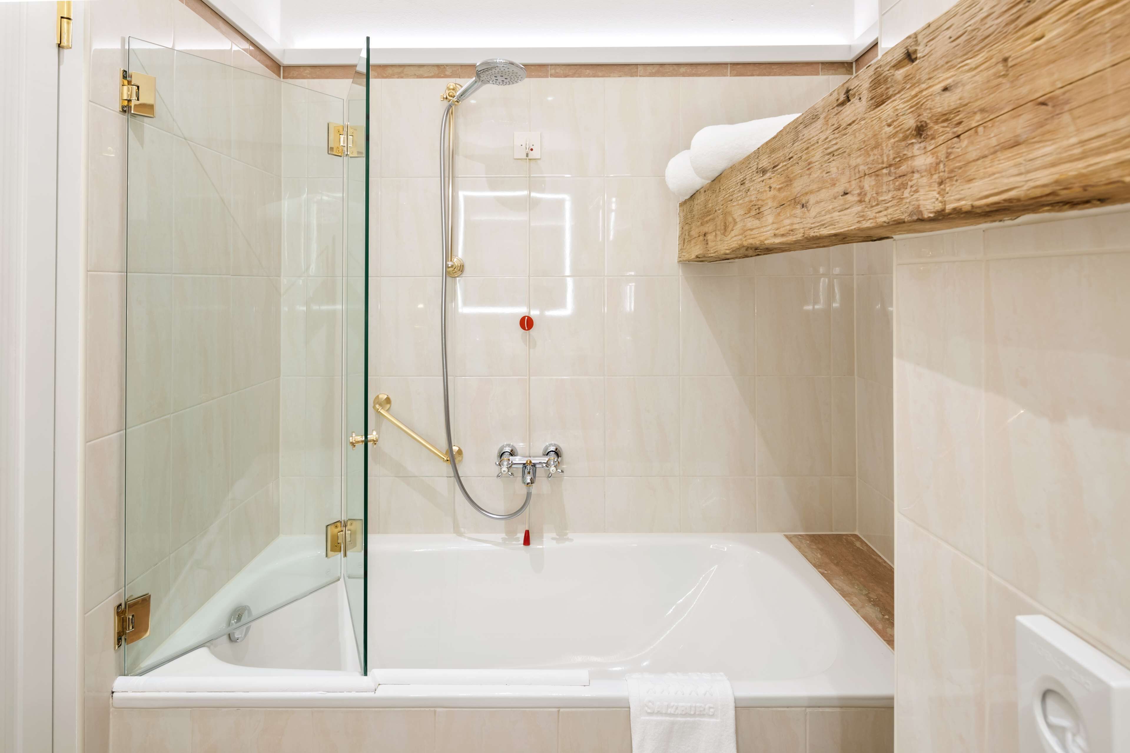 Un baño con ducha de vidrio, una bañera blanca y un estante de madera sobre la bañera.