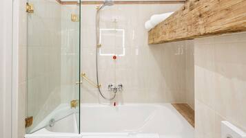 Un baño con ducha de vidrio, una bañera blanca y un estante de madera sobre la bañera.