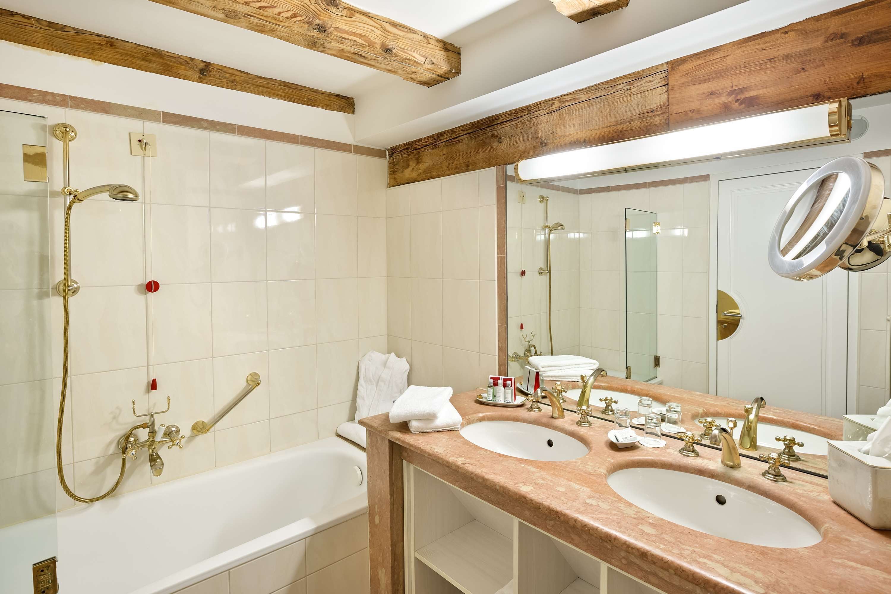 Une salle de bain avec une baignoire, deux lavabos, un grand miroir et une douche dotée d’un robinet doré.