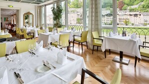 A restaurant with multiple tables set for dining, large windows offering a view of the city, and a modern interior design. - Radisson Blu Hotel Altstadt (Salzburg)