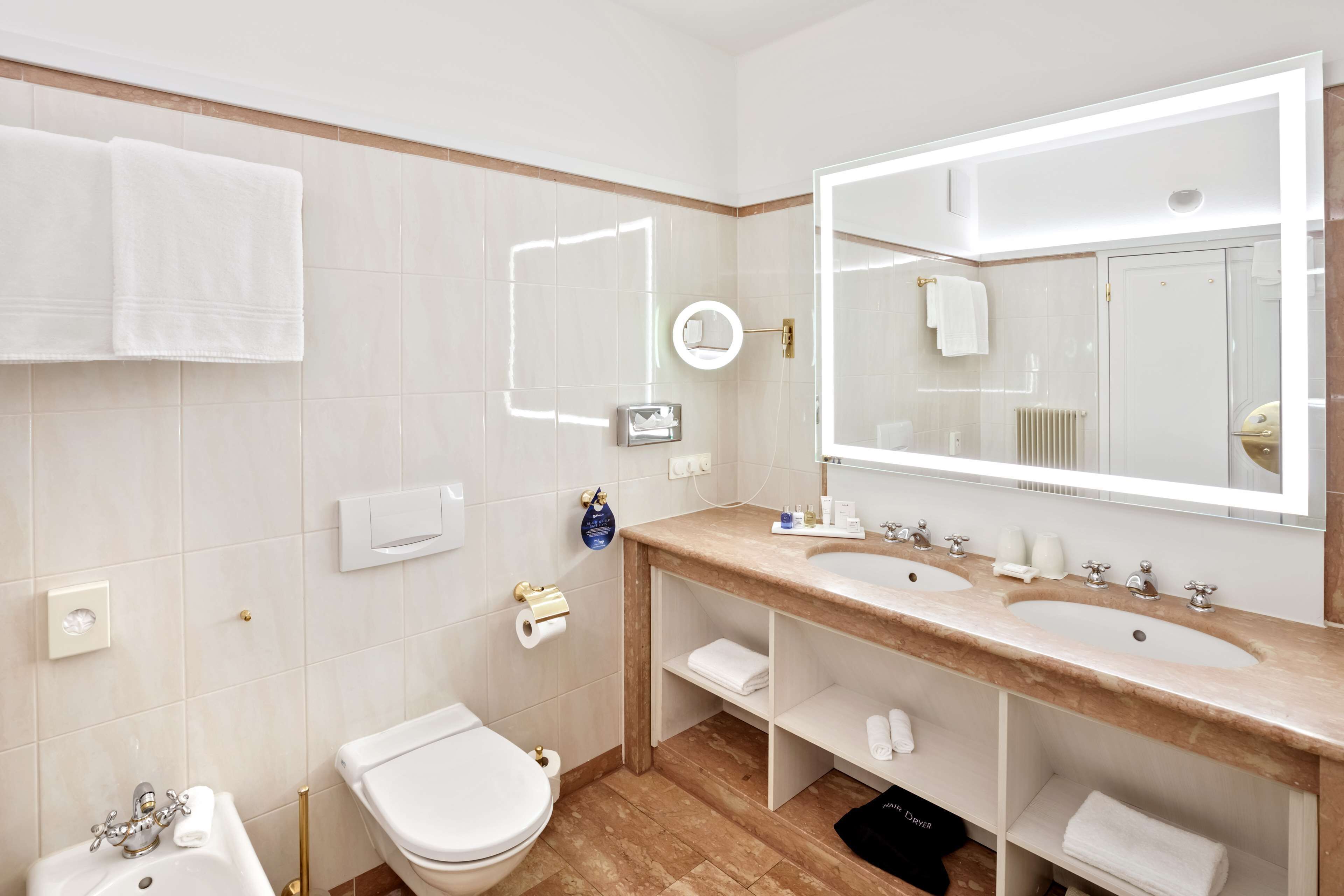 A modern bathroom with a double sink vanity, a toilet, and a large mirror.