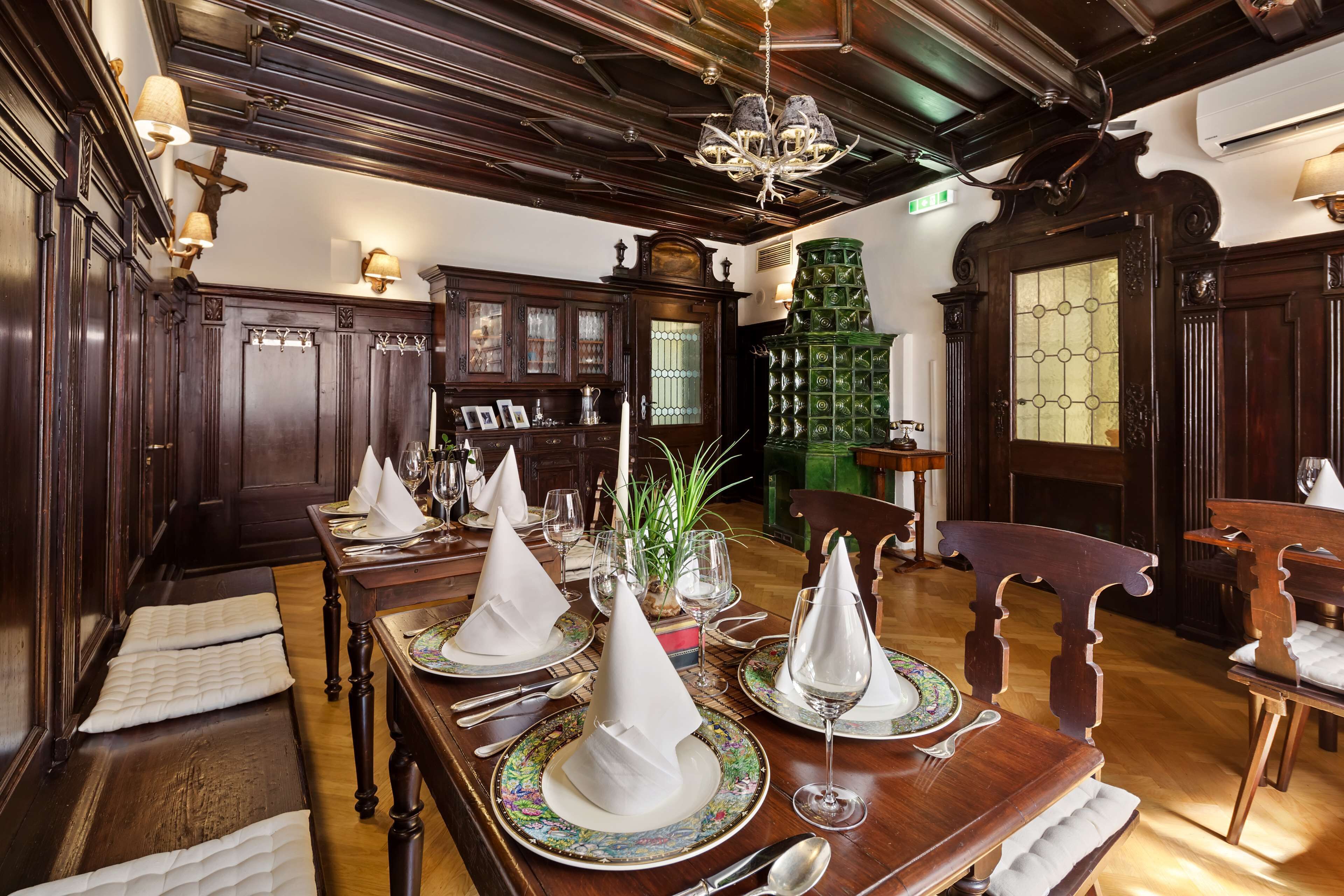 Un espace repas avec une longue table en bois dressée pour le repas, entourée de boiseries sombres et surmontée d’un lustre.