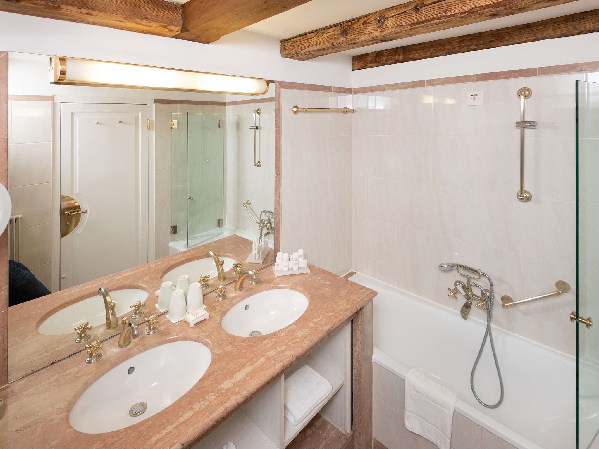 A bathroom with two sinks, a glass shower enclosure, and a wooden ceiling beam.