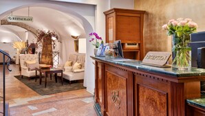 A reception area with a wooden desk, a sign reading "RECEPTION," and a vase with pink flowers. - Radisson Blu Hotel Altstadt (Salzburg)