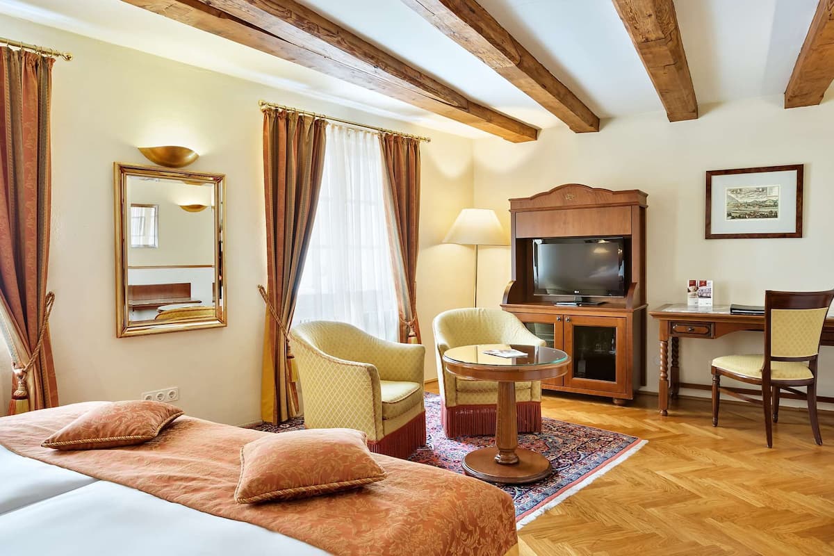 A hotel room with a bed, a desk with a TV, a chair, and a lamp.