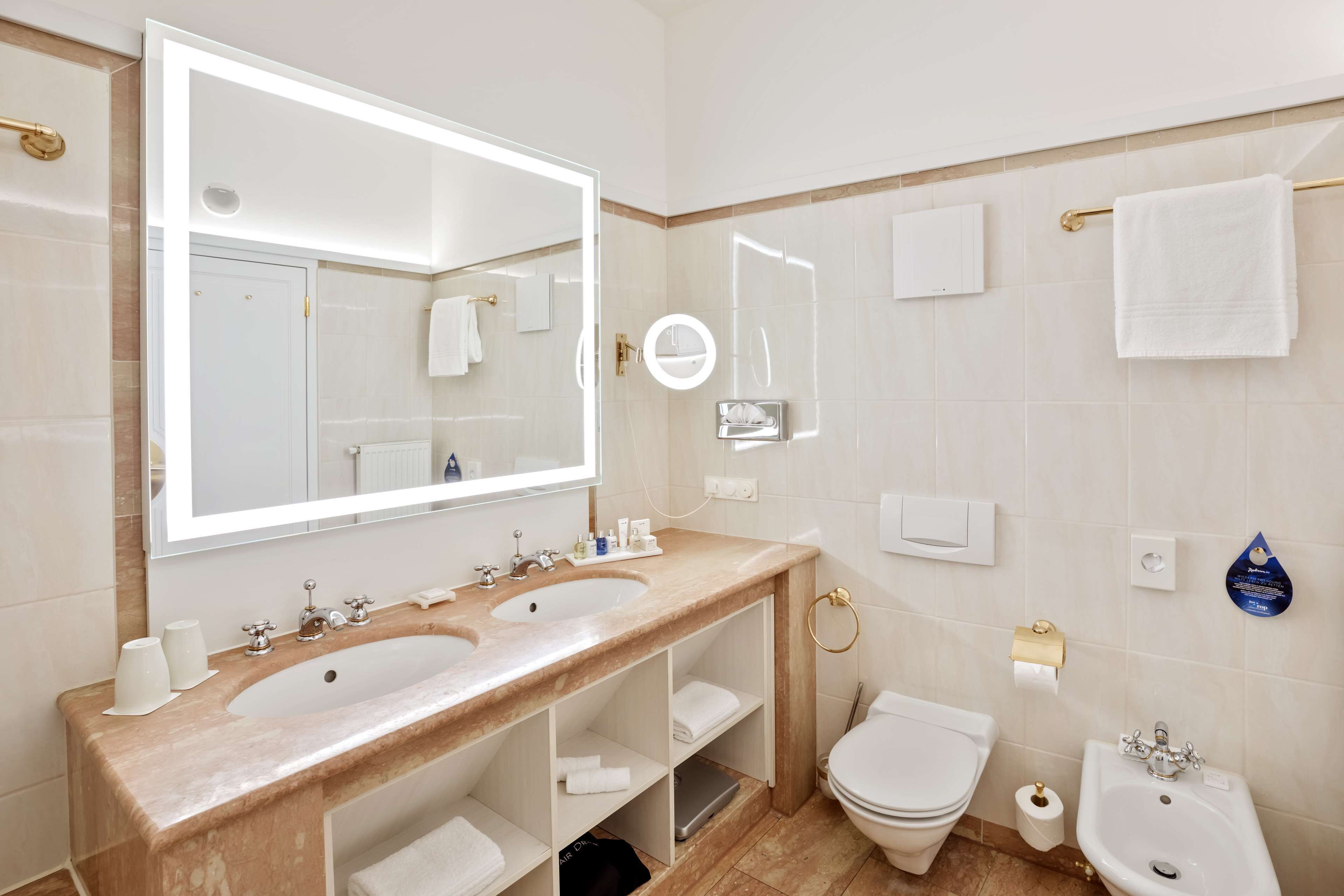 A modern bathroom with a double sink, a large mirror, a toilet, a bidet, and a vanity with shelves.
