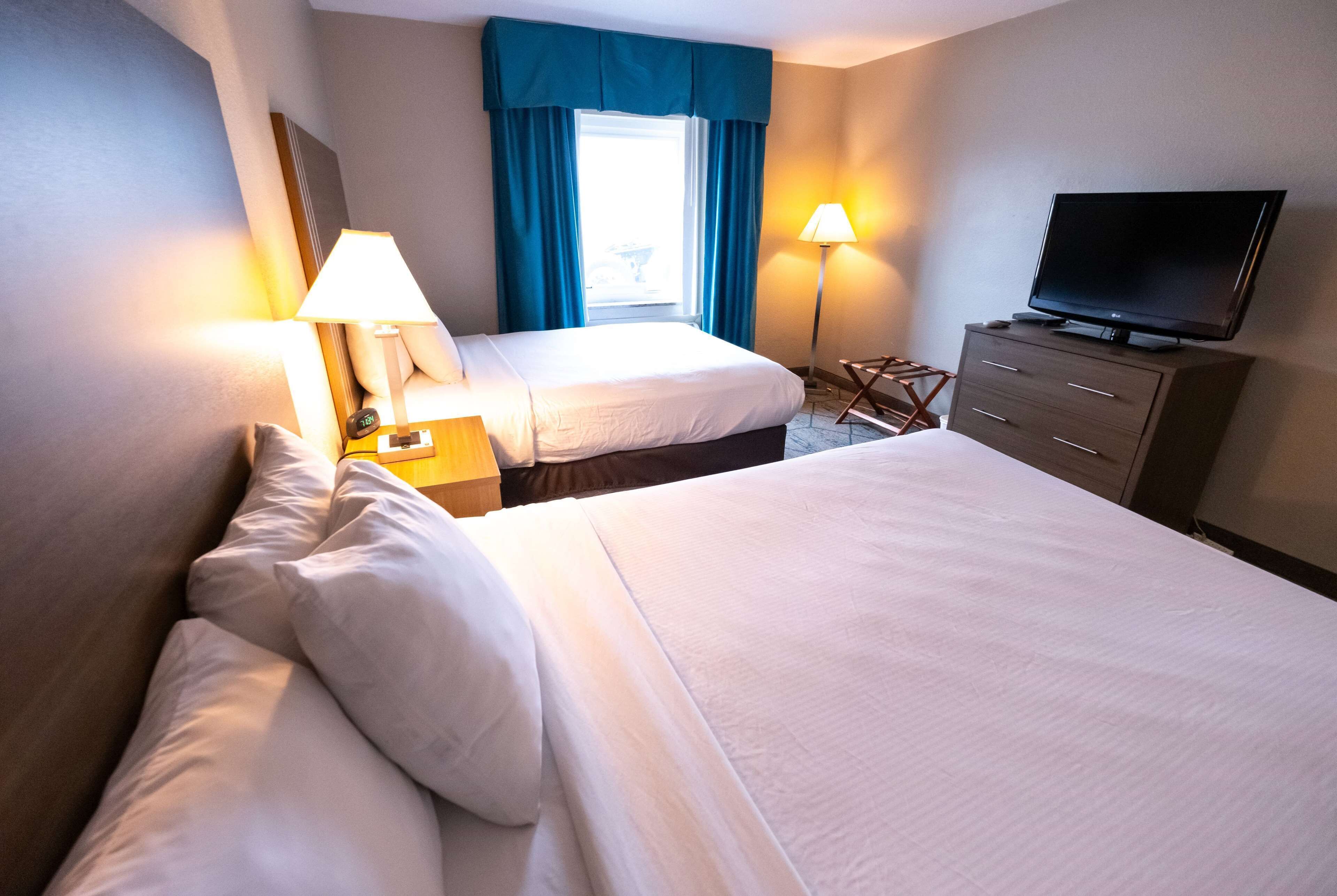 A hotel room with two beds, a TV on a dresser, and two lamps.