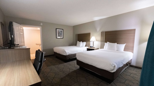 Quarto de hotel com duas camas, uma escrivaninha, uma cadeira, uma televisão e um abajur.
