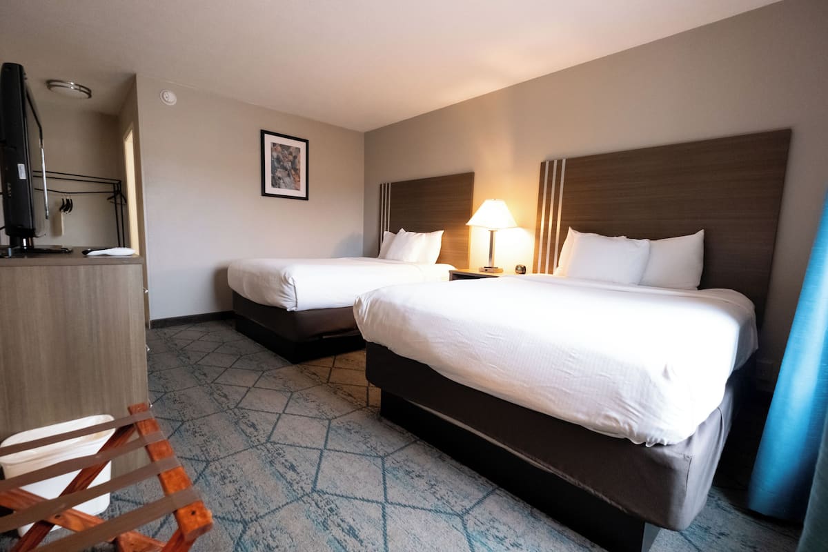 A hotel room with two beds, a desk with a computer, a chair, and a lamp.