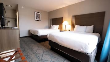 A hotel room with two beds, a desk with a computer, a chair, and a lamp.