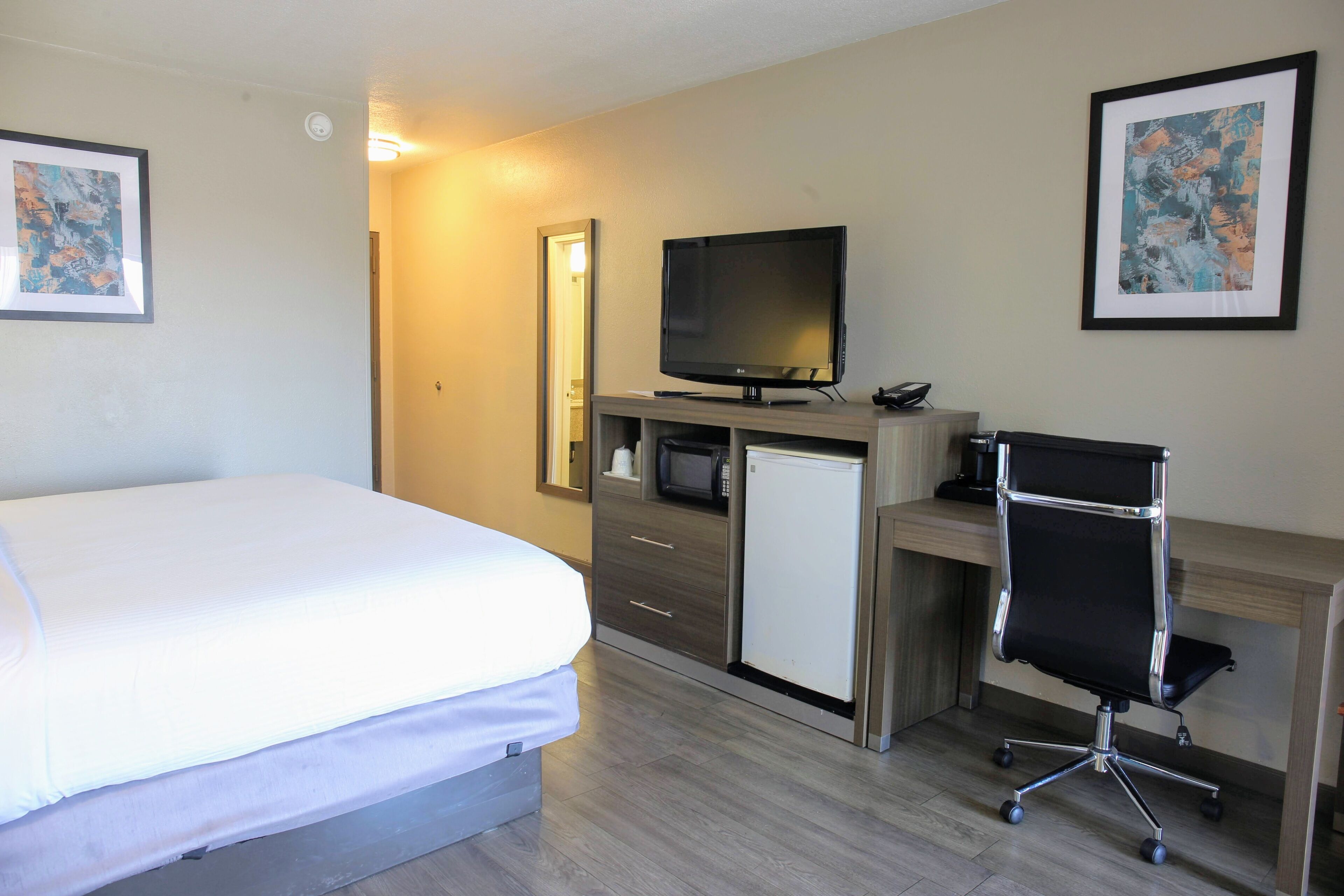 Ett hotellrum med en säng, ett skrivbord med en dator, en tv och en mikrovågsugn.
