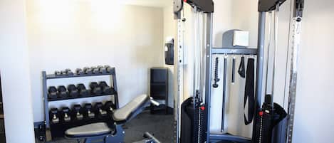 Une salle de sport équipée de matériel de musculation, d’un banc et d’un porte-haltères.