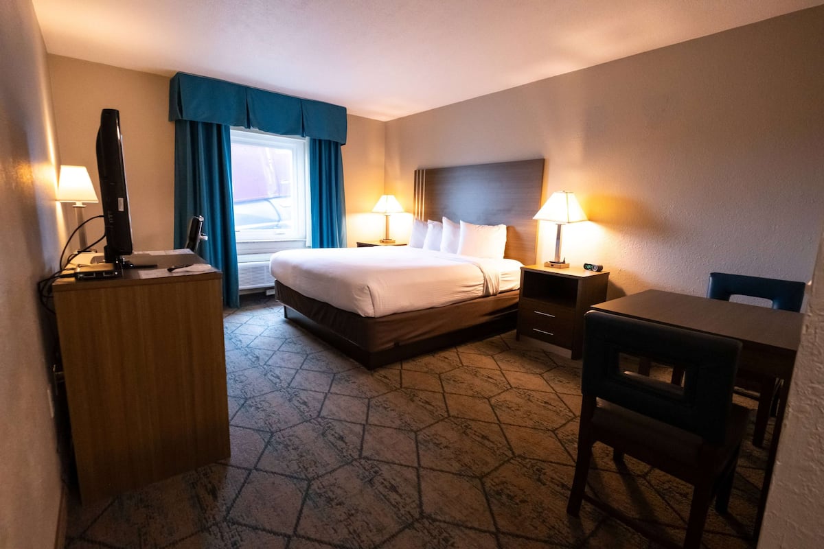 A hotel room with a bed, two bedside tables with lamps, a desk, and a television on a stand.