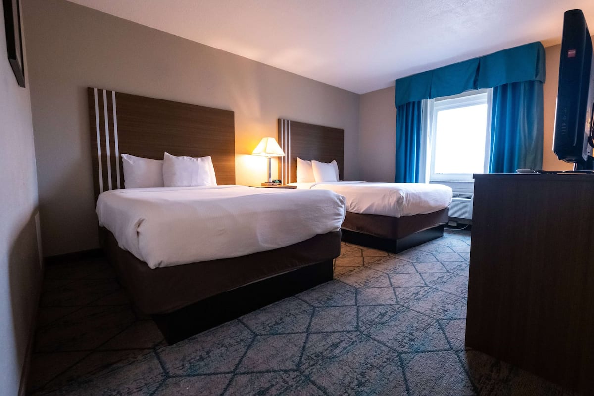 A hotel room with two beds, a desk, a lamp, and a television.