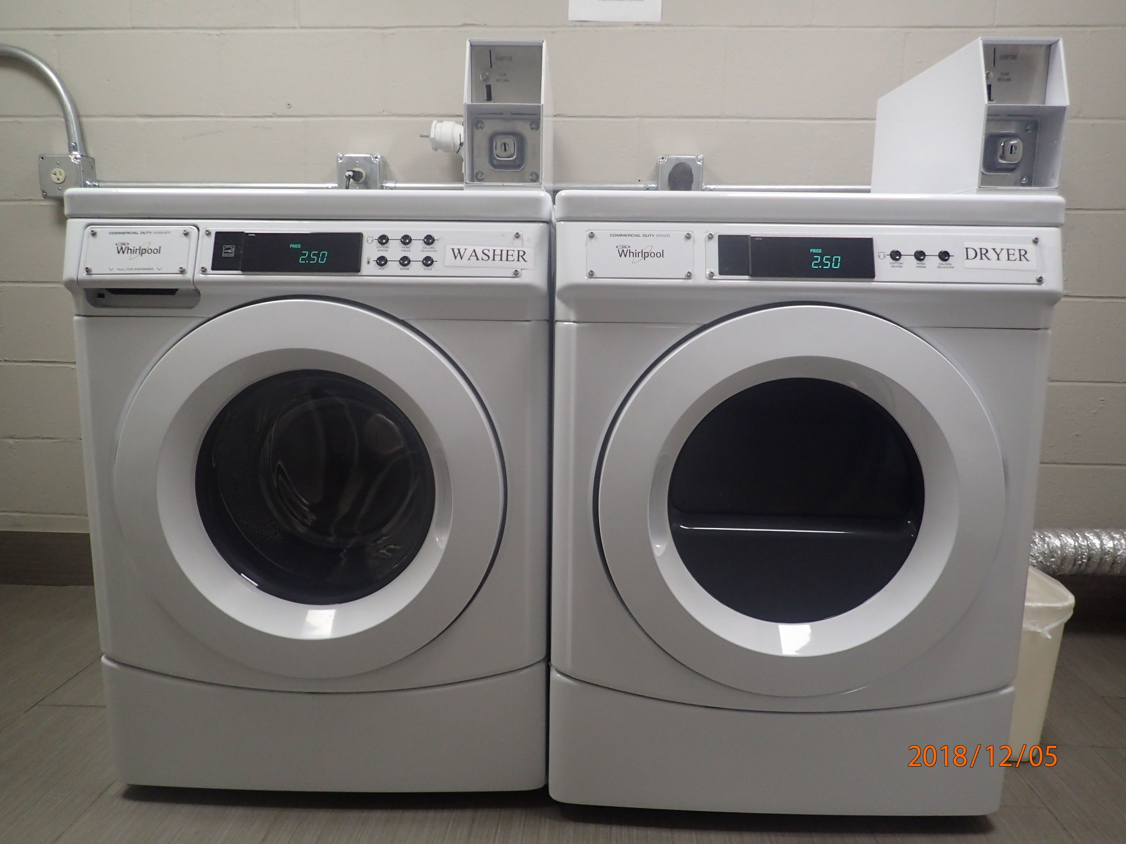 Dos lavadoras Whirlpool de uso comercial una al lado de la otra en un cuarto de servicio.