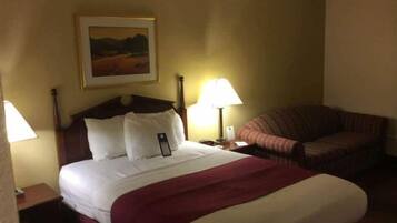 A hotel room with a bed, a nightstand, a lamp, a chair, and a painting on the wall.