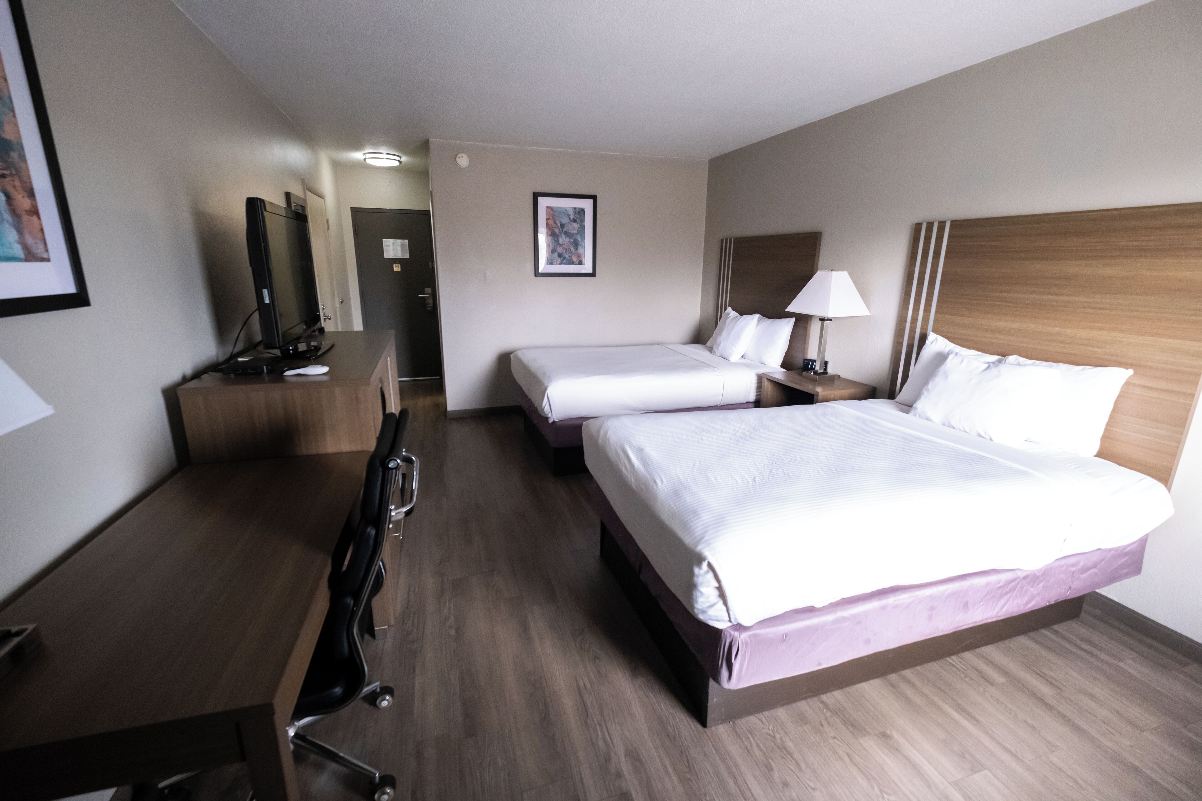 A hotel room with two beds, a desk with a computer, a chair, and a TV.