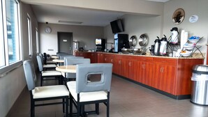 Cozinha moderna com espaço para café, área de estar com mesas e cadeiras, e um relógio na parede.