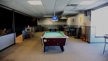 A pool table in a room with a carpeted floor, a ceiling light, and a wall-mounted speaker.
