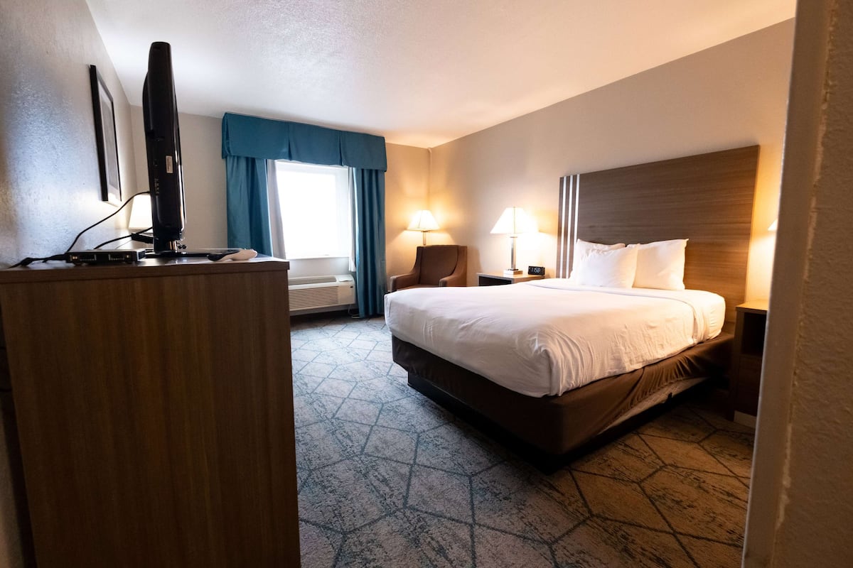 A hotel room with a bed, a desk with a computer, a chair, and a lamp.