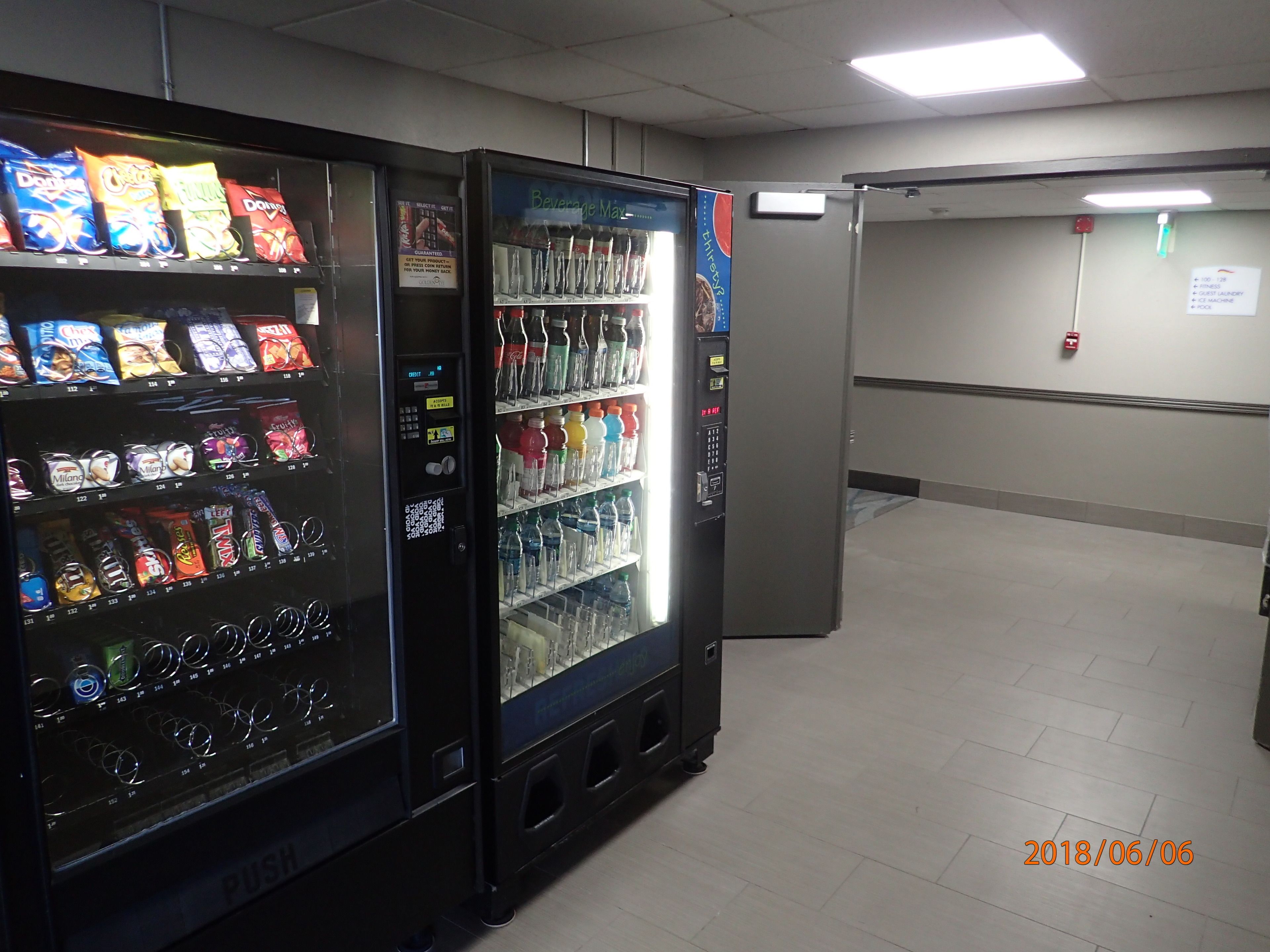 A vending machine area with snack and drink options, a fire alarm, and a sign indicating guest laundry services.