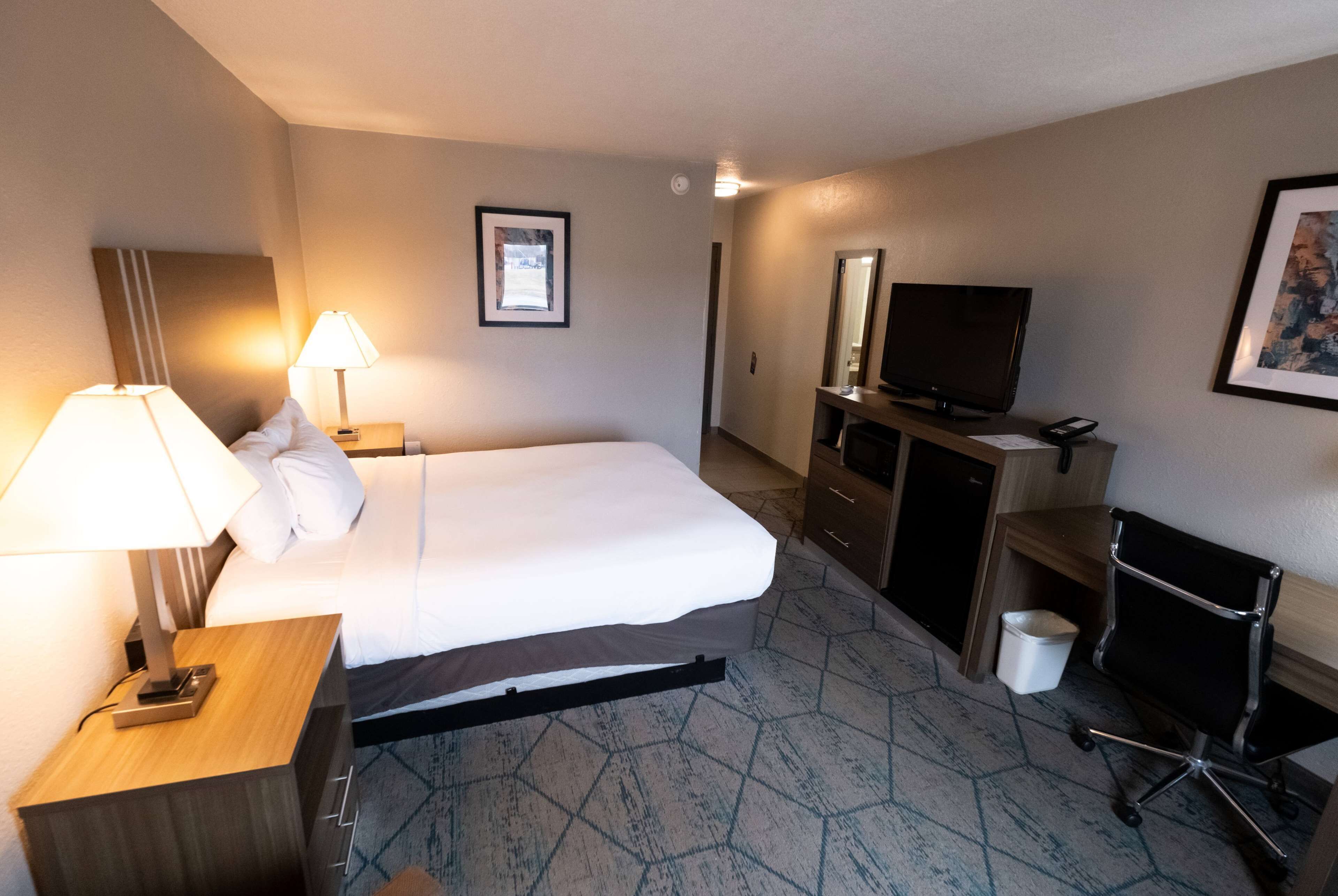 Una camera d'albergo con un letto, abat-jour, televisore, una scrivania e una sedia.