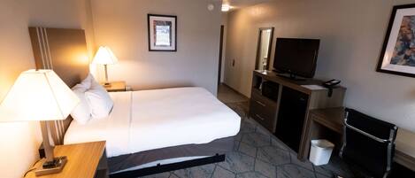 A hotel room with a bed, bedside lamps, a TV, a desk, and a chair.