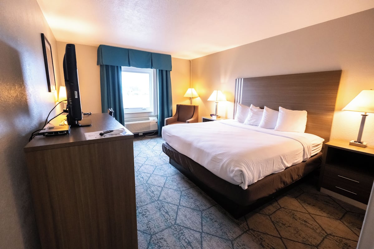 A hotel room with a large bed, a desk with a computer, two bedside lamps, and a window with curtains.