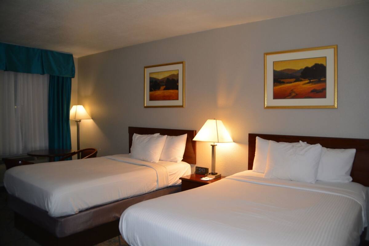 A hotel room with two beds, a nightstand with a lamp, and two framed pictures on the wall.