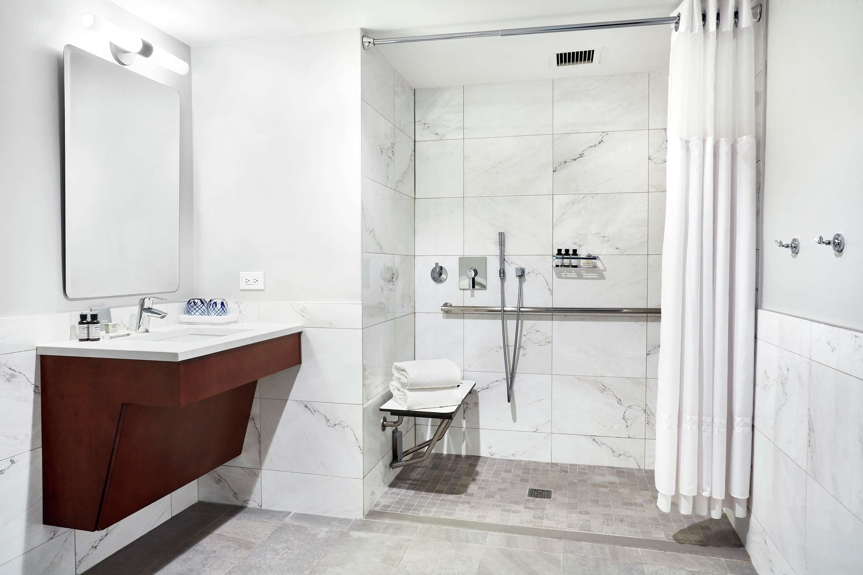A modern bathroom with a marble shower, a vanity with a mirror, and a towel rack.