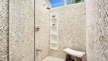 Un baño moderno con paredes de mosaicos, cabina de ducha de vidrio y un pequeño tocador de madera.