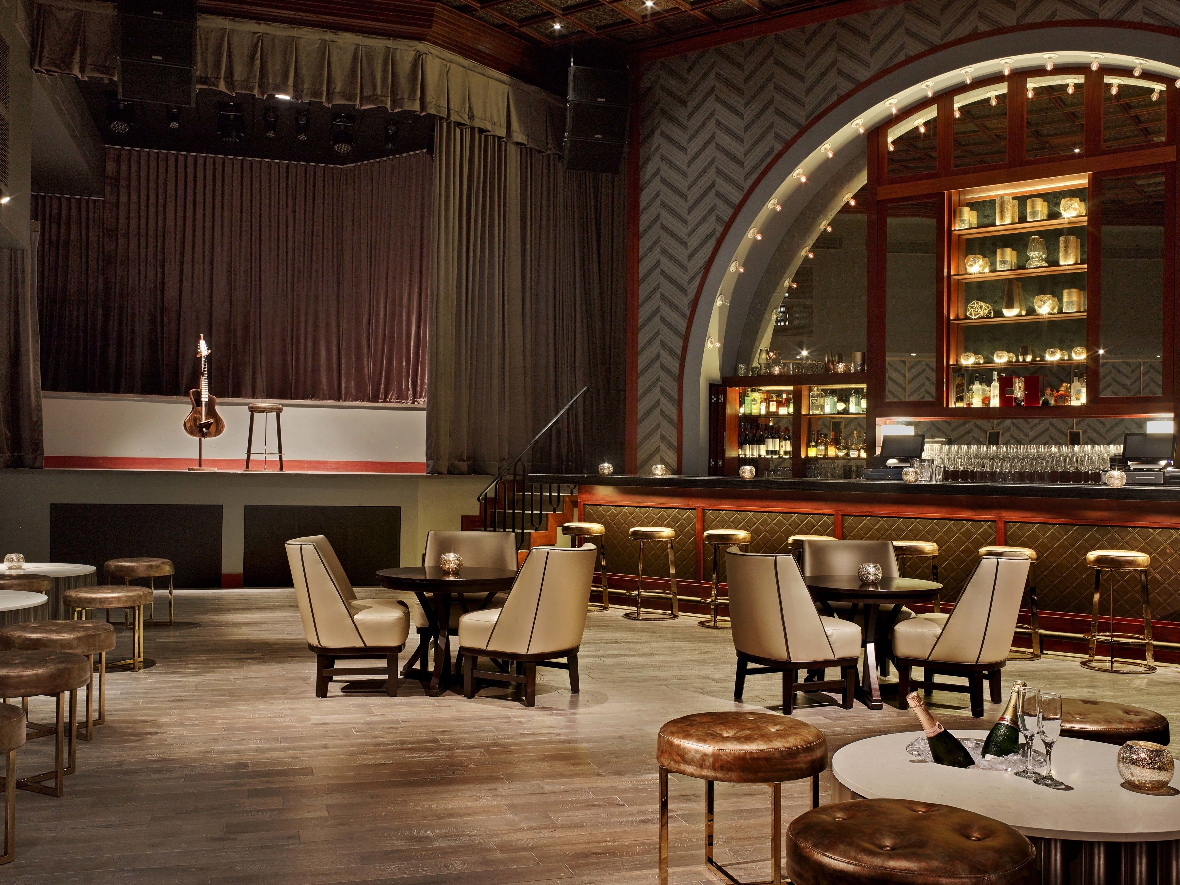A bar area with a stage, bar stools, and a seating area with tables and chairs.