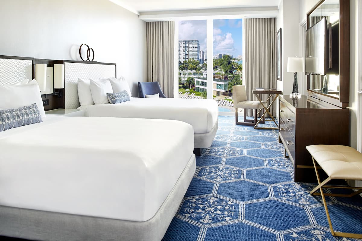 Une chambre d’hôtel avec deux lits, un bureau, une chaise, une grande fenêtre donnant sur la ville et une moquette à motifs.