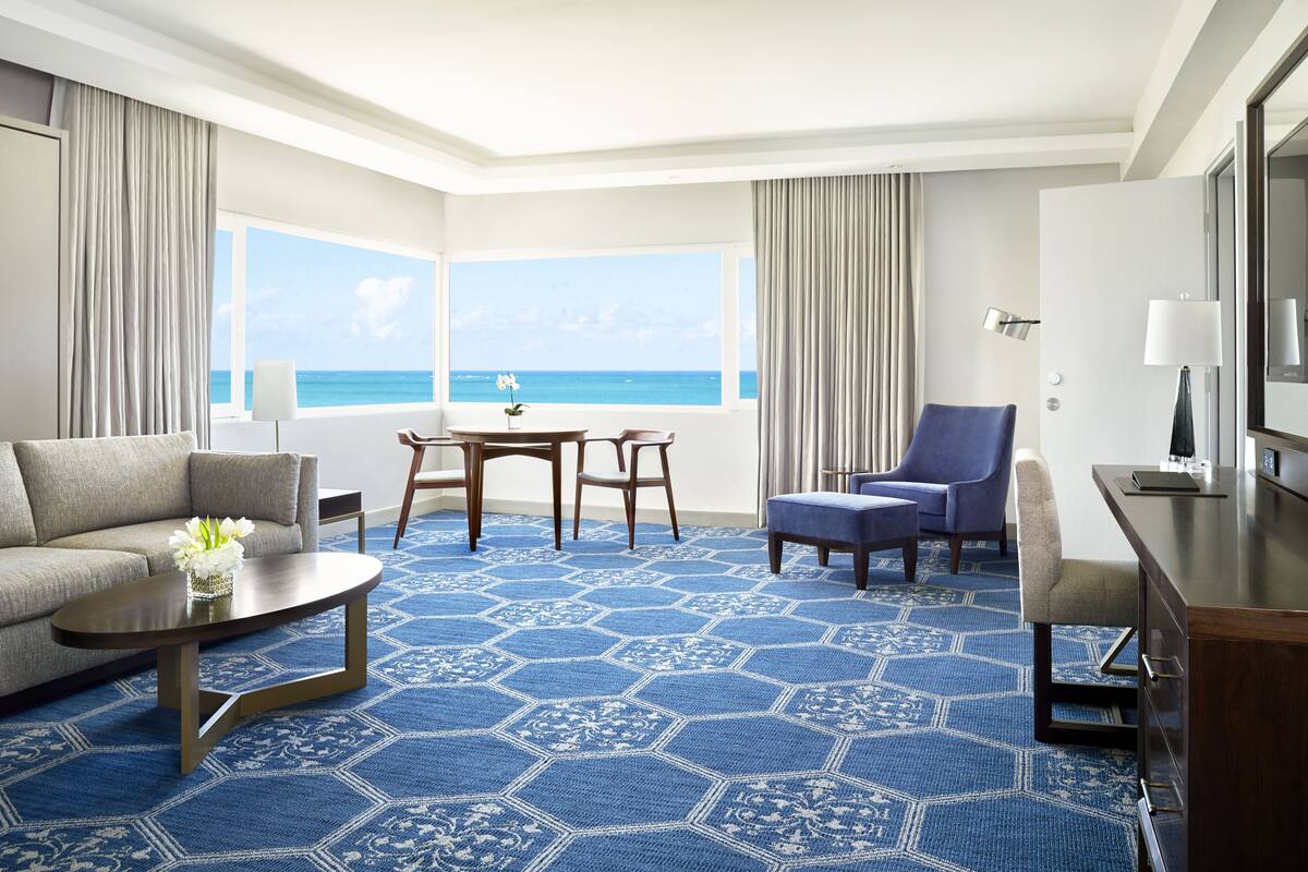 Une chambre d’hôtel dotée d’une grande fenêtre donnant sur l’océan, d’un canapé, d’une table basse, d’un bureau et d’une chaise.