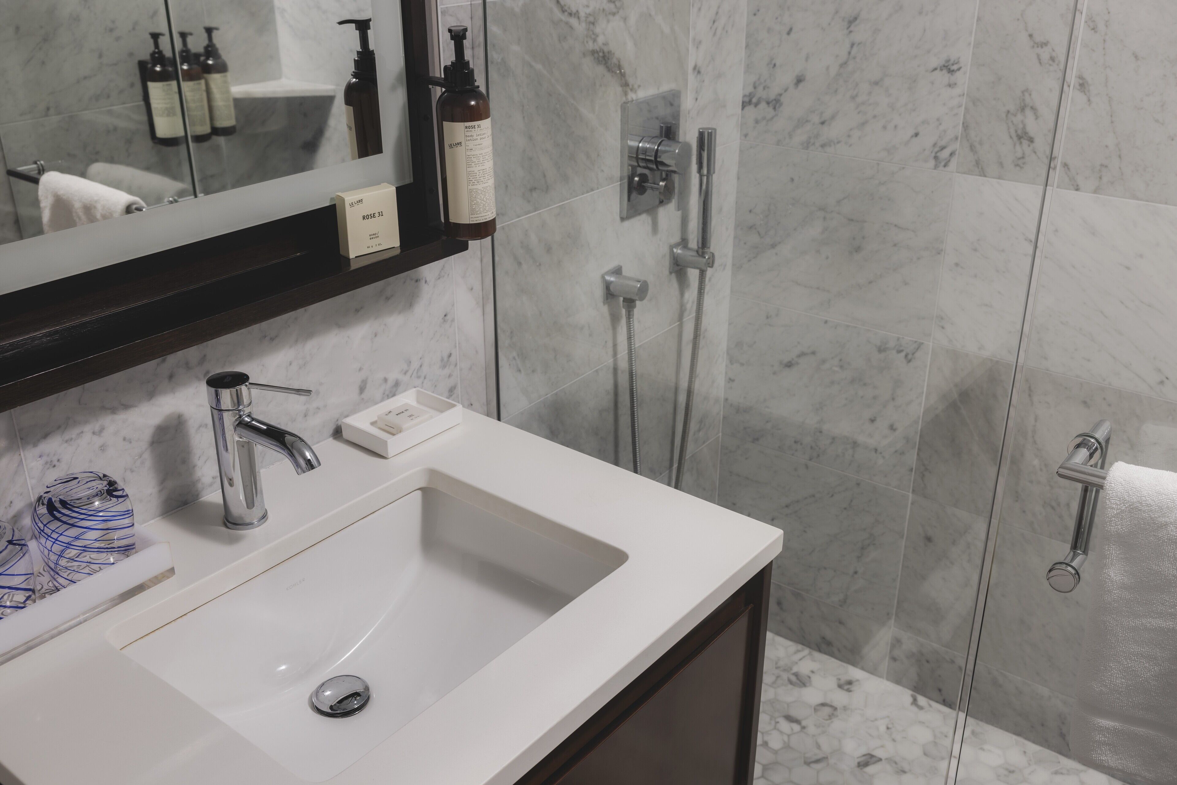 A bathroom with a white sink, a mirror, a shower, and a towel rack.