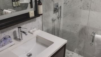 A bathroom with a white sink, a mirror, a shower, and a towel rack.