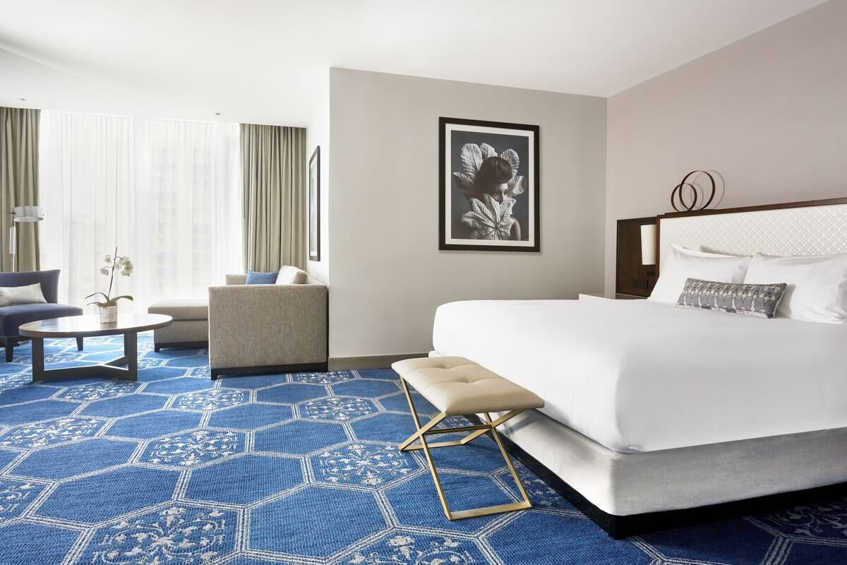 Une chambre d’hôtel avec un grand lit, un canapé, une petite table et une grande fenêtre avec des rideaux.