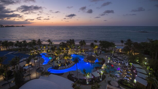 Ein Resort mit großem Schwimmbad, Liegebereichen und Blick auf das Meer im Abendlicht.